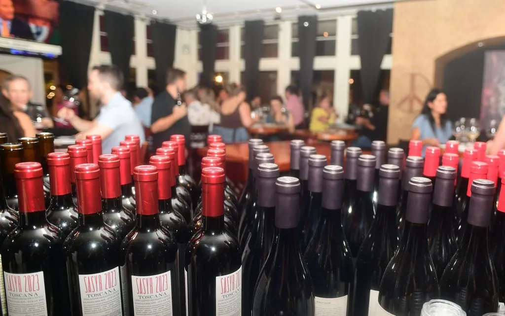 Bottles of Toscana red wine in the foreground with guests gathered at a wine club event behind them