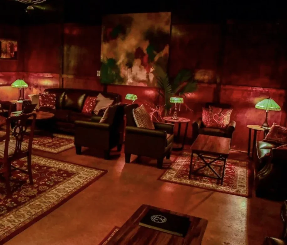 The Hideout's lounge, lit in deep red, with leather armchairs, a sofa, Persian rugs, and green Tiffany-style lamps
