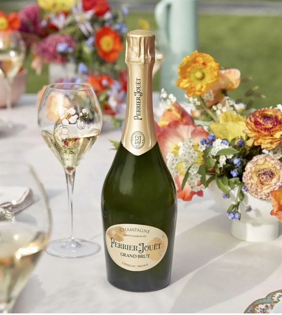 A bottle of Perrier-Jouët Grand Brut champagne and a flute on a table set with spring flowers