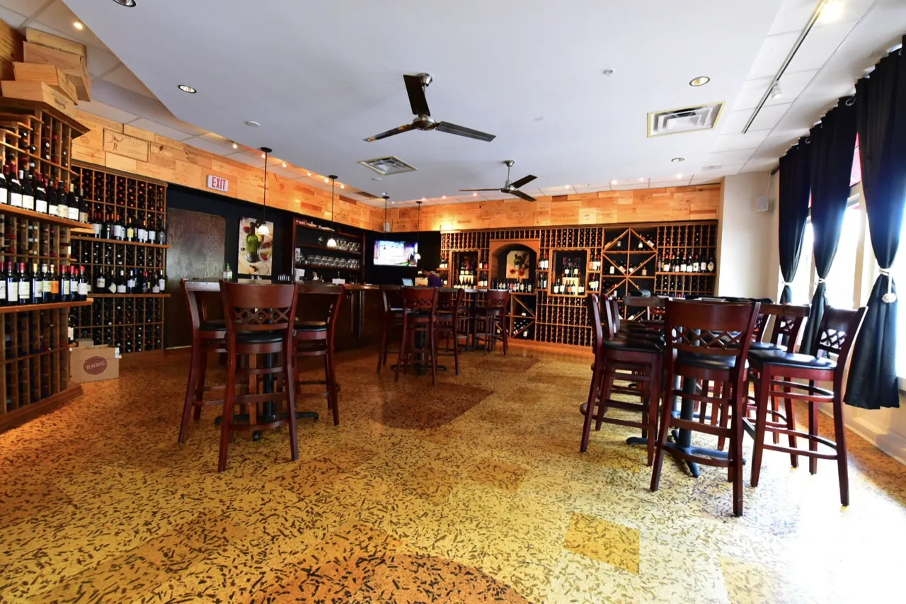 The main floor of the wine bar, with high-top tables, wine racks, and the bar at the back