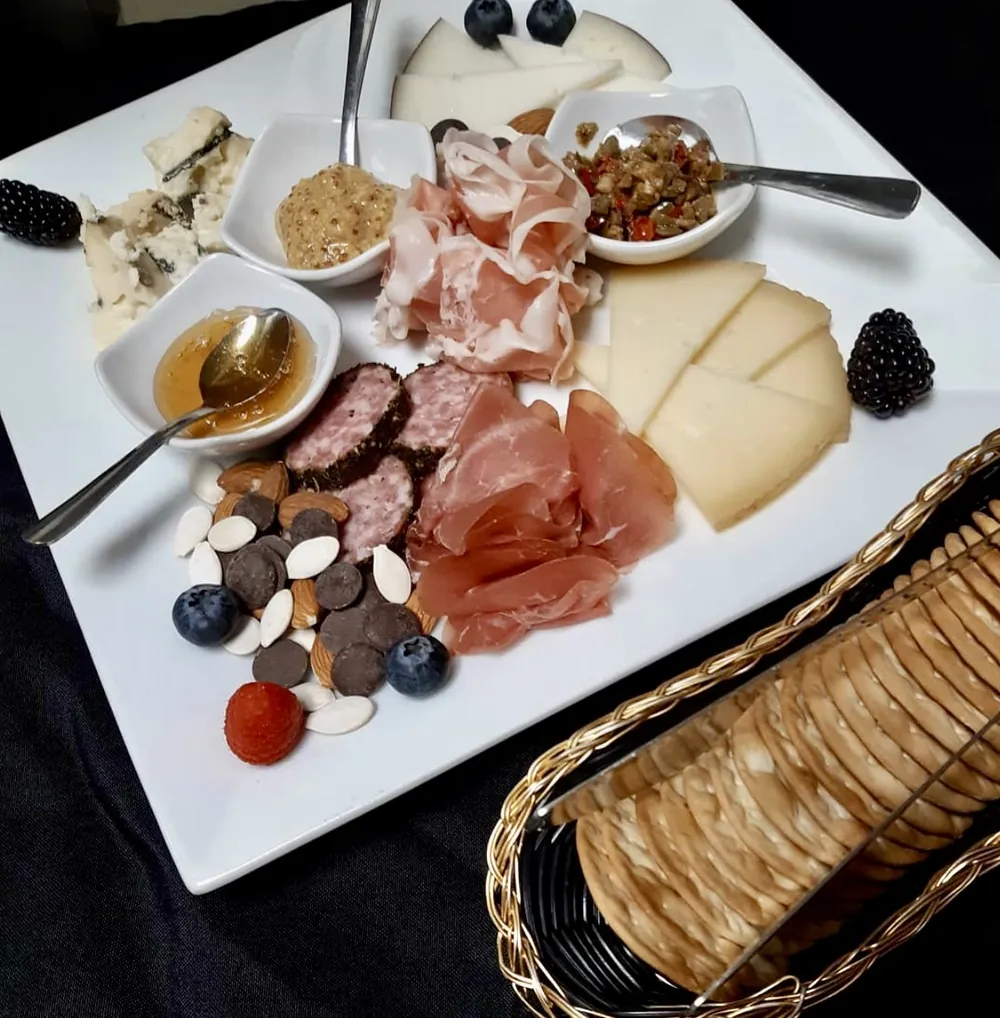 A charcuterie board with cured meats, cheeses, honey, mustard, olive relish, nuts, and berries, with a basket of crackers